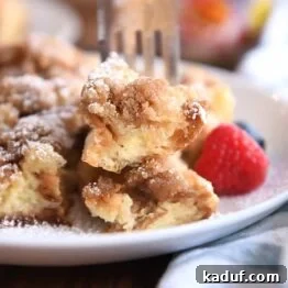 Fork skewering two bites of baked French toast on white plate.