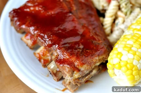 Slow-Roasted Tender Ribs 2 A rack of perfectly cooked, glazed BBQ ribs on a white plate, served with fresh corn on the cob and a vibrant pasta salad, showcasing their irresistible tenderness.
