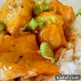 Close-up of golden brown baked orange chicken pieces in a bowl, glistening with sauce.