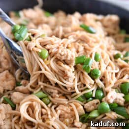 Effortless Fiery Garlic Ramen 11 Tong grabbing scoop of ramen noodles with peas, ground turkey and green onions.