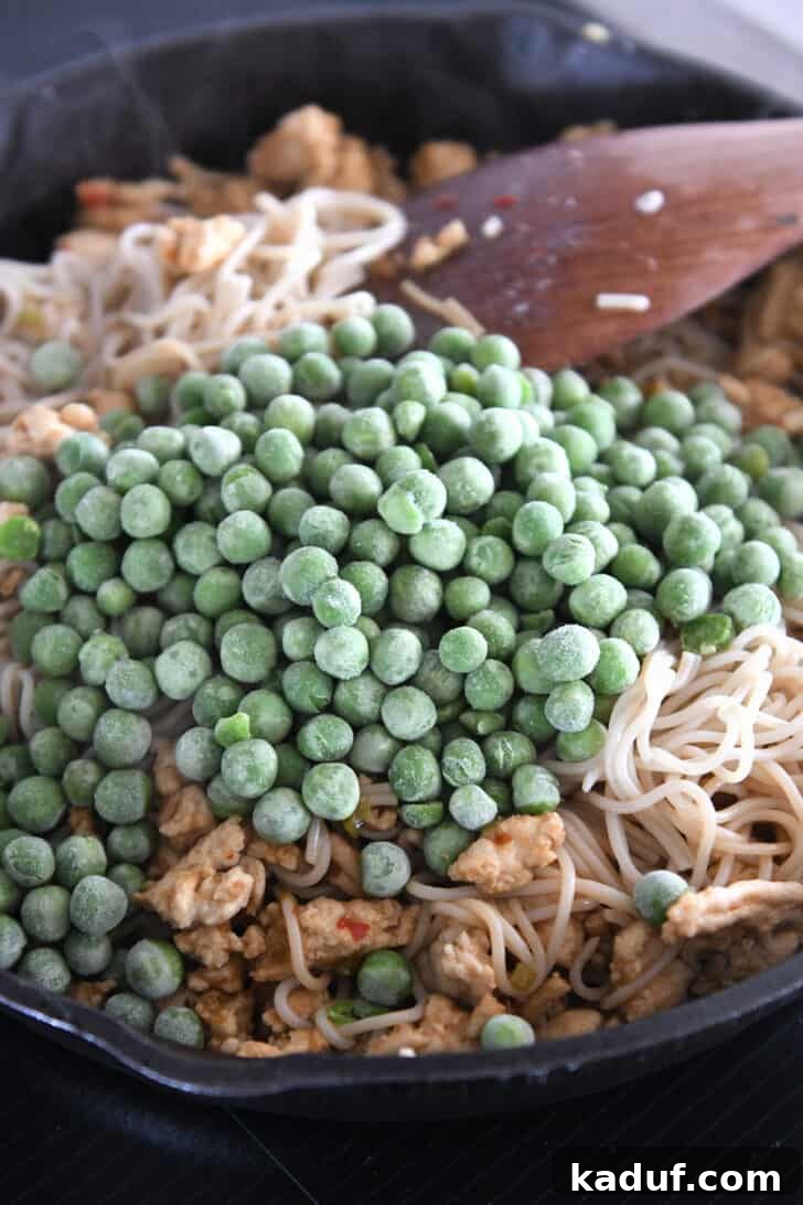 Effortless Fiery Garlic Ramen 7 Frozen peas in cast iron skillet with ramen noodles.