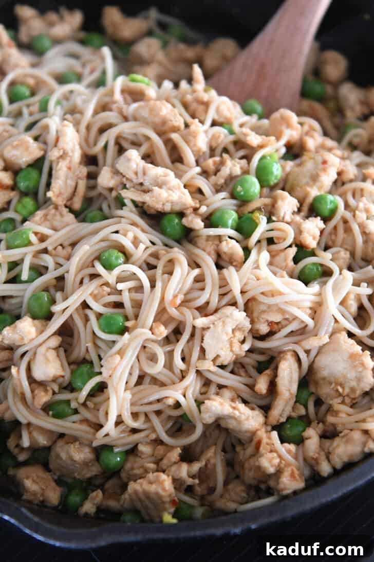 Effortless Fiery Garlic Ramen 8 Stirring ramen noodles in cast iron skillet with frozen peas and ground turkey.
