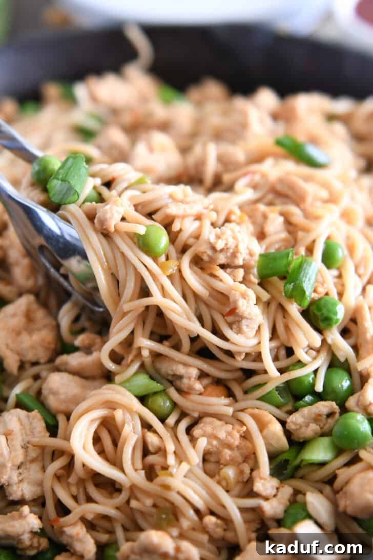 Effortless Fiery Garlic Ramen 9 Tongs grabbing scoop of ramen noodles with peas and green onions.