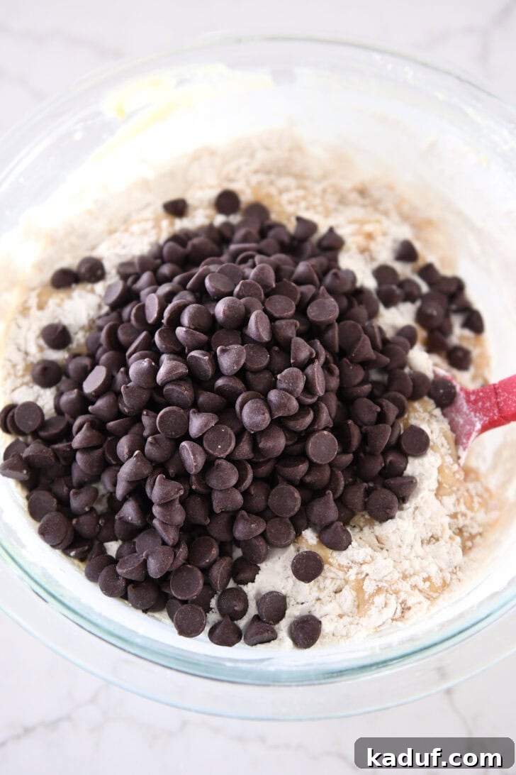 Abundant chocolate chips are folded into the thick, rich brown butter muffin batter in a glass bowl.