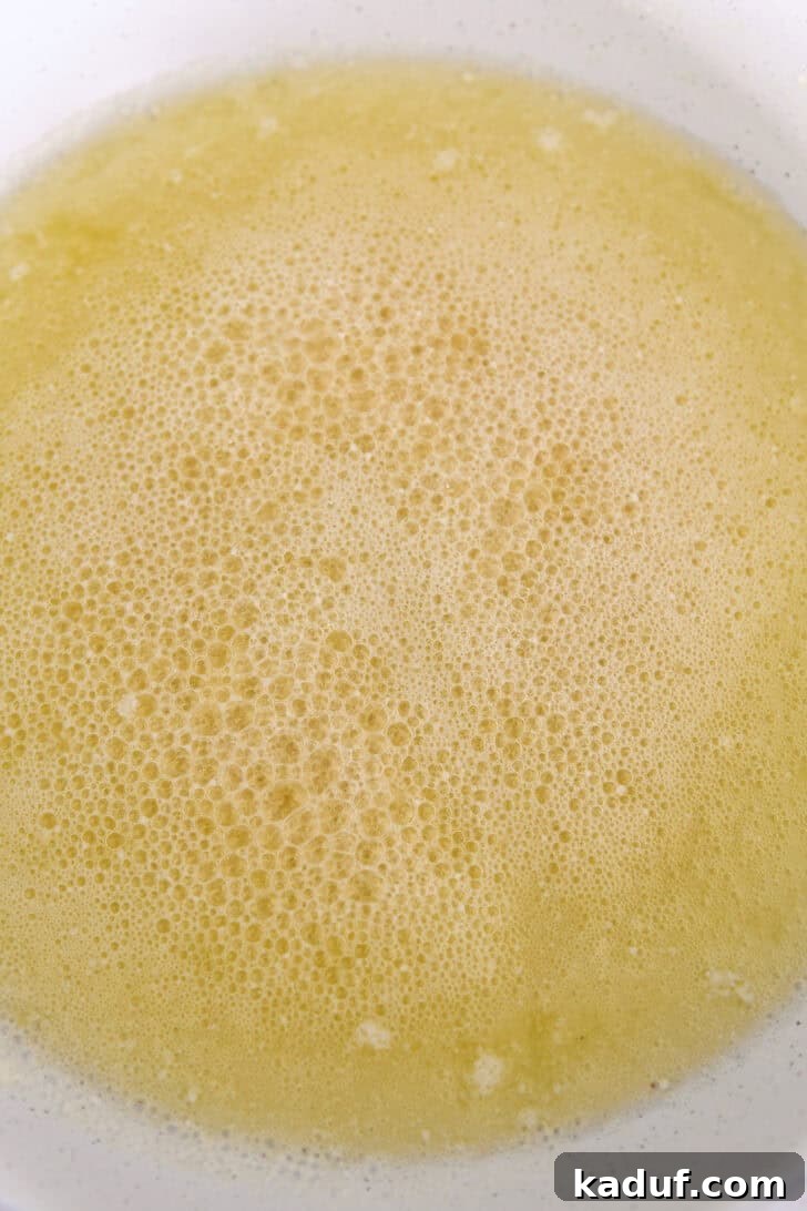 Butter actively browning in a white skillet, with milk solids beginning to toast and turn golden.