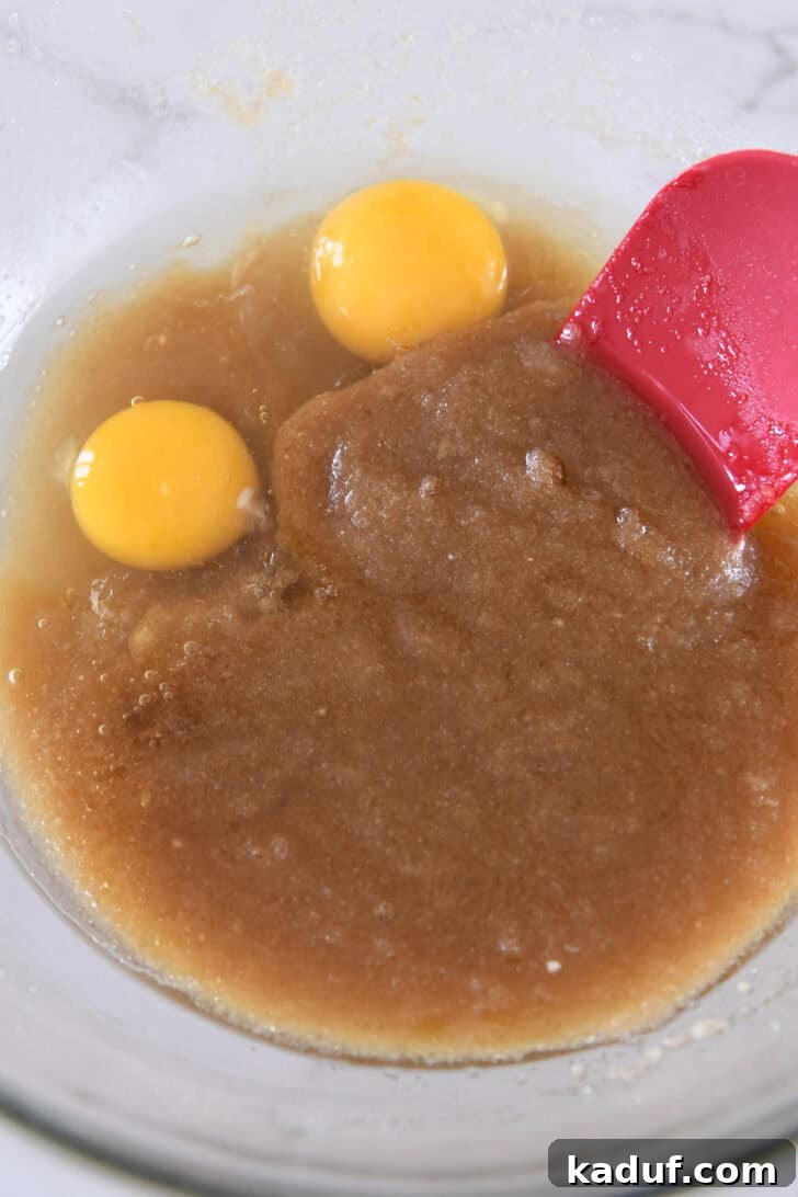 Fresh eggs are cracked into the sugary brown butter mixture in a glass bowl, ready for blending.