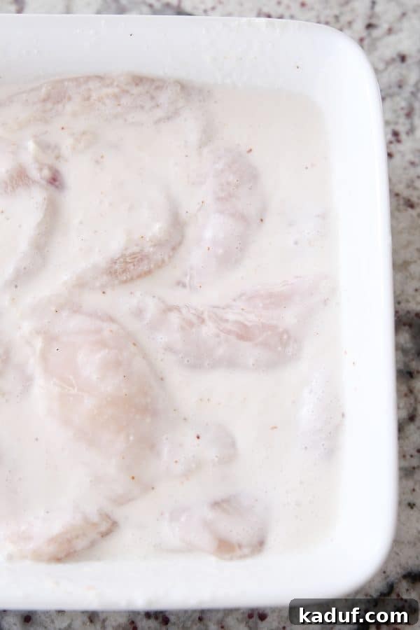Caramel Coconut Chicken 7 A white casserole dish filled with chicken pieces fully submerged in a creamy, off-white marinade, waiting to infuse with flavors in the refrigerator.