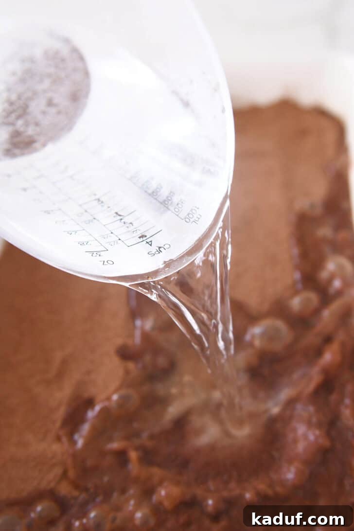 Boiling water being carefully poured over the sugar and cocoa-covered cake batter, initiating the pudding formation process.