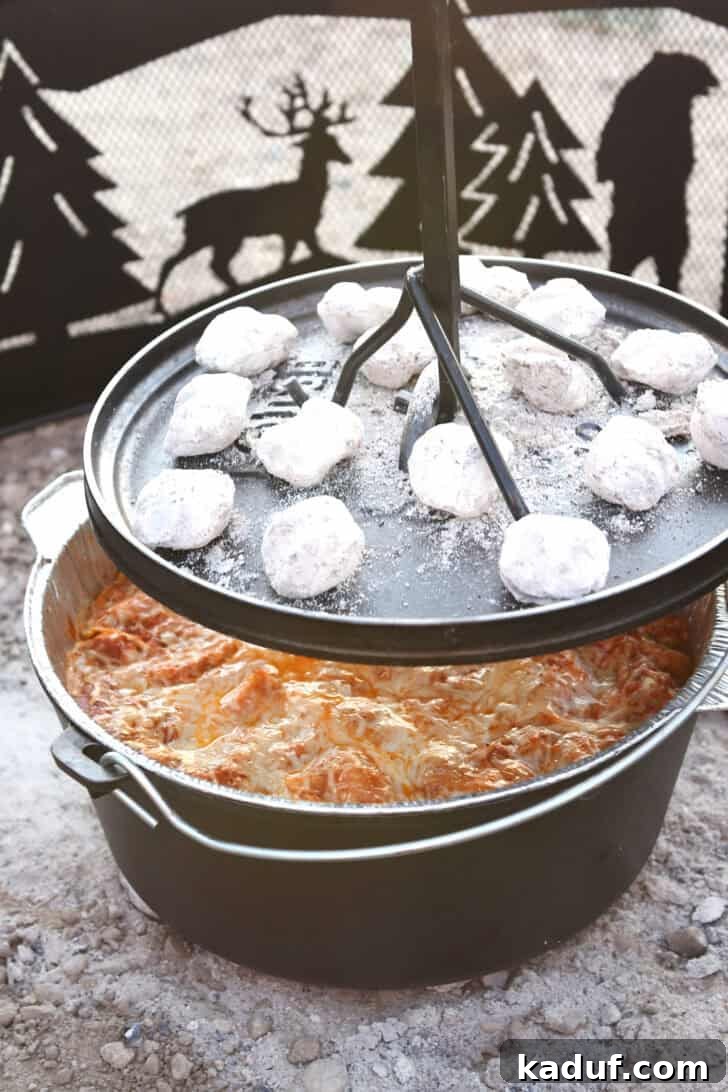 Hearty Dutch Oven Lasagna 15 Lifting lid from Dutch oven with coals on top, revealing steaming lasagna.