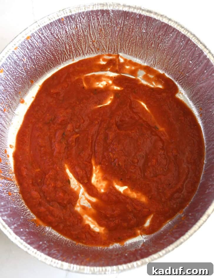 Hearty Dutch Oven Lasagna 5 Top down view of pasta sauce spread on bottom of Dutch oven liner for lasagna.