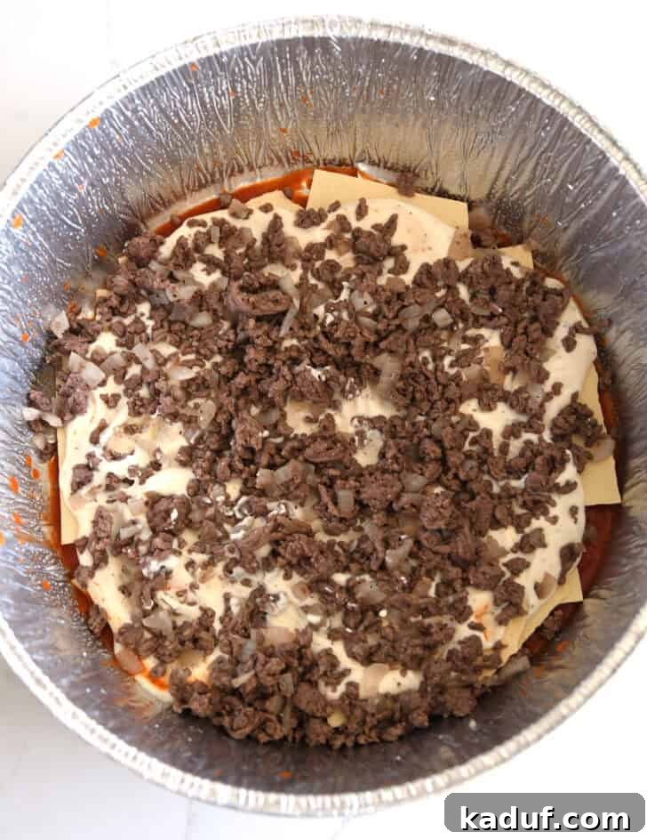 Hearty Dutch Oven Lasagna 8 Top down view of ground beef and cooked onions layered in Dutch oven liner.