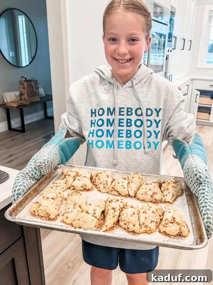 Friday Thoughts: A Brain Dump 7 A young girl proudly holding a tray laden with freshly baked, golden-brown cinnamon scones, ready to be served.