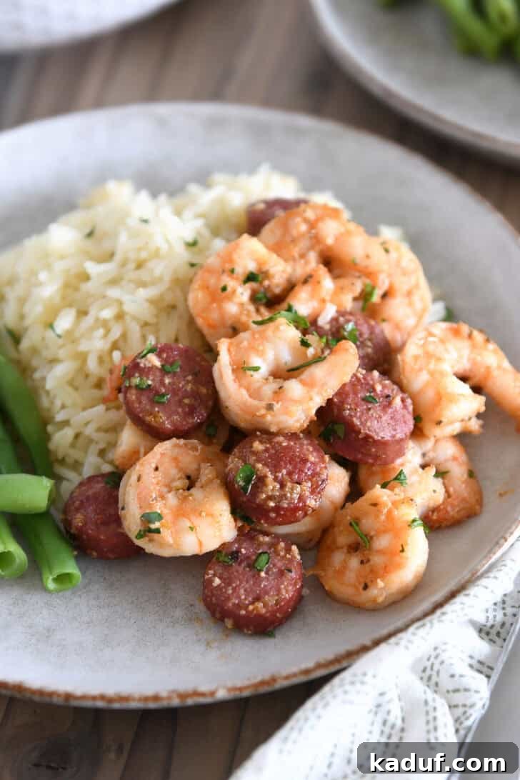 A gray stone plate featuring a generous serving of garlic butter shrimp and sausage alongside fluffy white rice, garnished with fresh parsley.