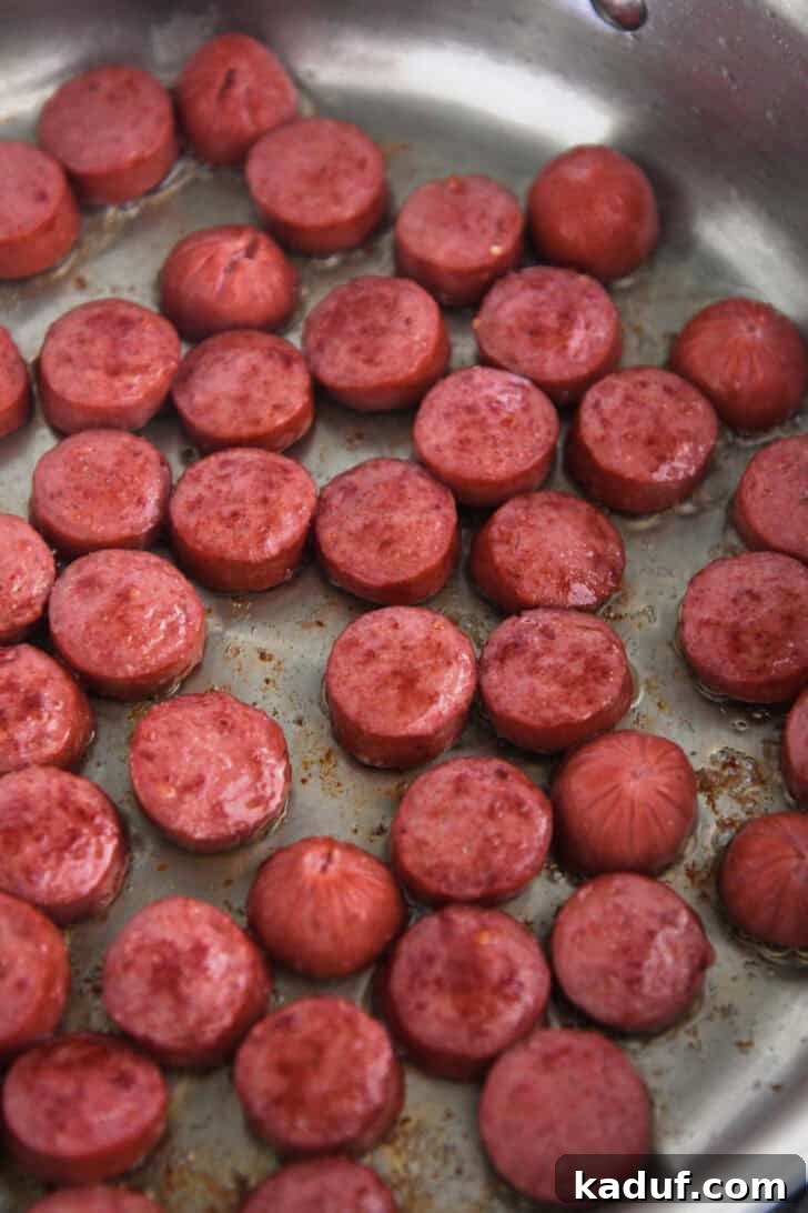 Slices of kielbasa sausage browning to a perfect golden crisp in a stainless steel saucepan, highlighting the first step of this easy recipe.