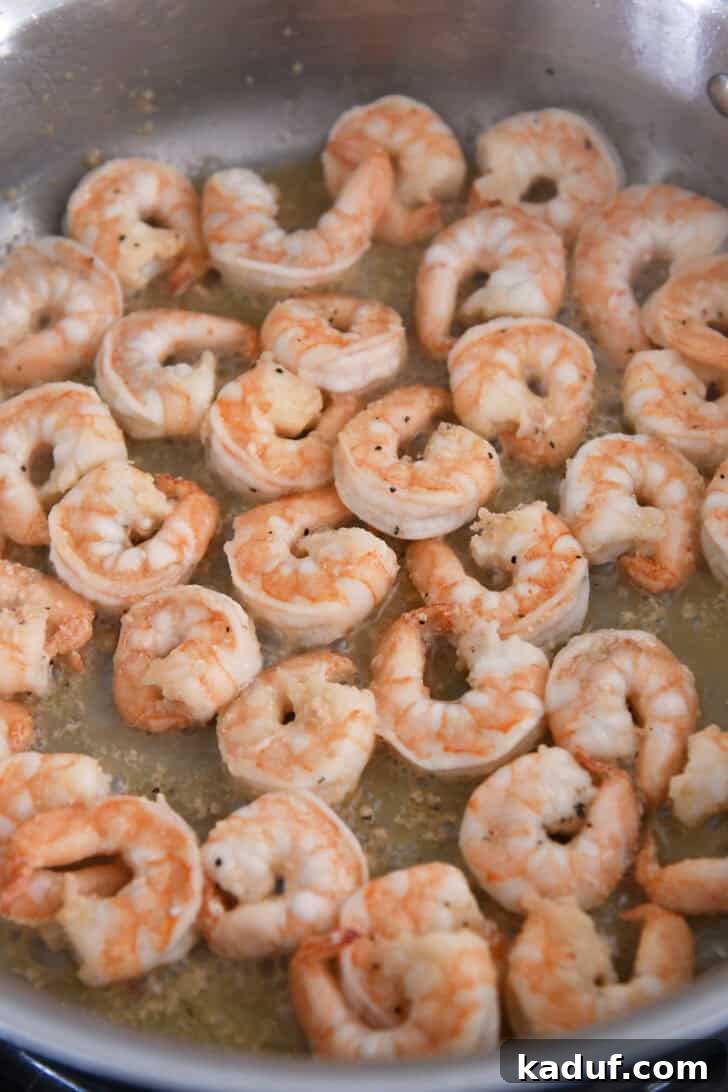 Fresh shrimp cooking in a shimmering pool of garlic butter within a stainless steel pan, turning pink as they absorb the delicious flavors.