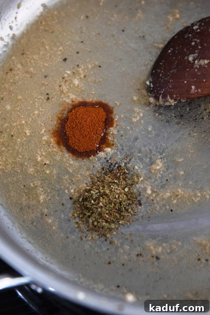 A close-up of a stainless steel skillet, filled with a rich blend of melted butter, fragrant minced garlic, and vibrant spices, ready for the next step.
