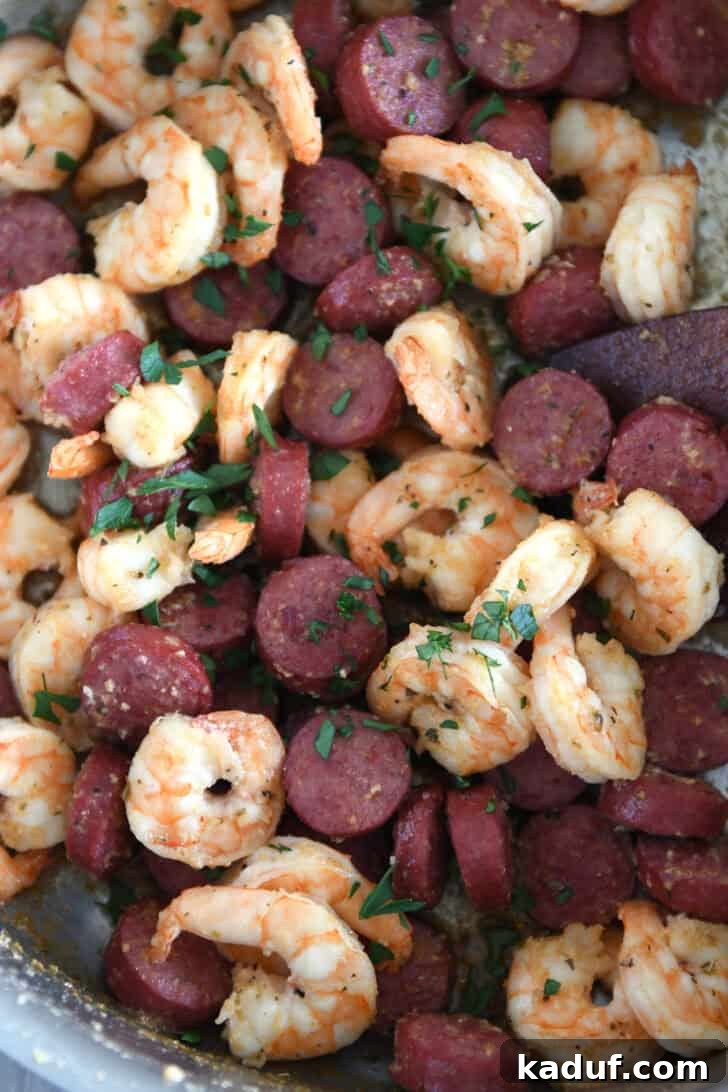 A stainless steel skillet brimming with perfectly cooked shrimp and sausage, glistening with garlic butter sauce, topped with a sprinkle of fresh green parsley.