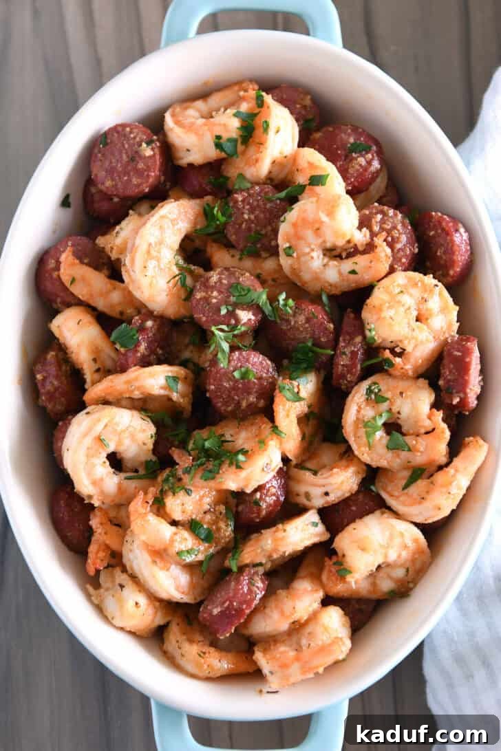 A top-down view of an elegant oval serving dish overflowing with cooked shrimp, sausage, and a vibrant sprinkle of fresh parsley, ready to be enjoyed.