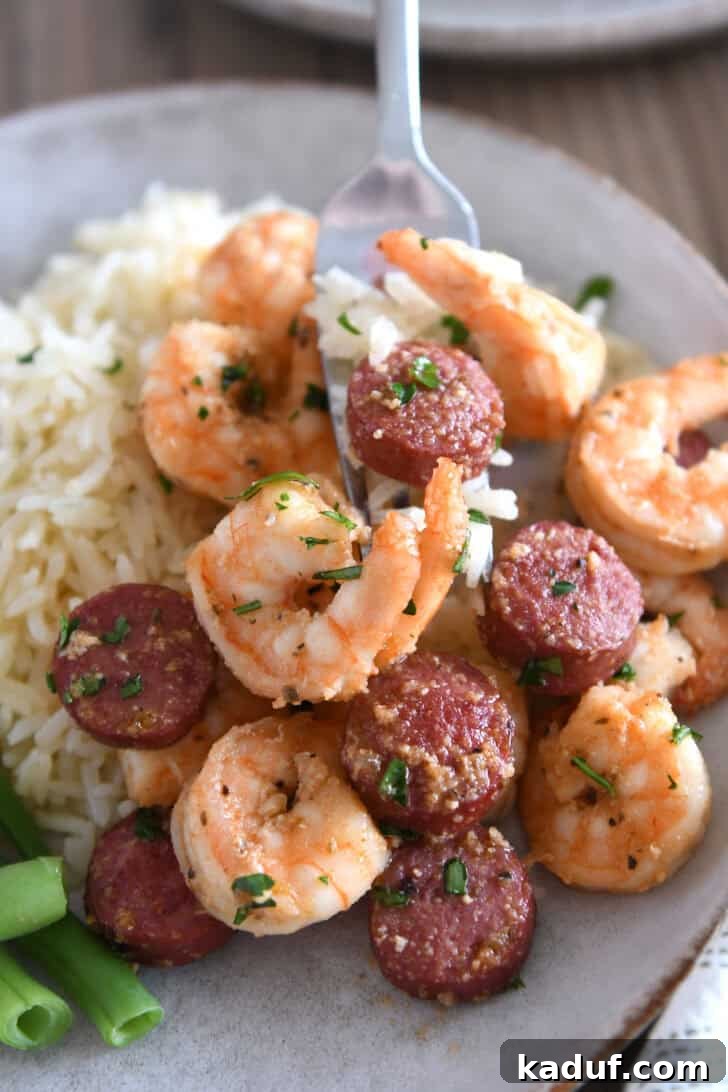A fork poised to scoop a perfect bite of garlic butter shrimp and sausage from a gray plate, showcasing the appetizing texture and vibrant colors of the dish.