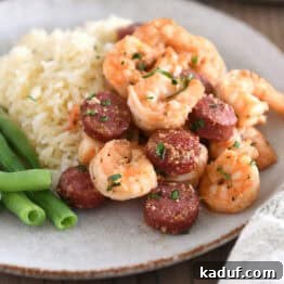 A gray plate with green beans, white rice, perfectly cooked shrimp and sausage, highlighting a balanced and delicious meal.