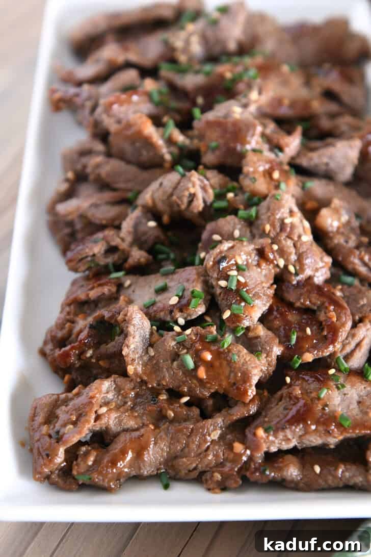 Simple Korean Beef Bulgogi 2 White tray piled with cooked pieces of thin beef, green onions, sauce and sesame seeds.