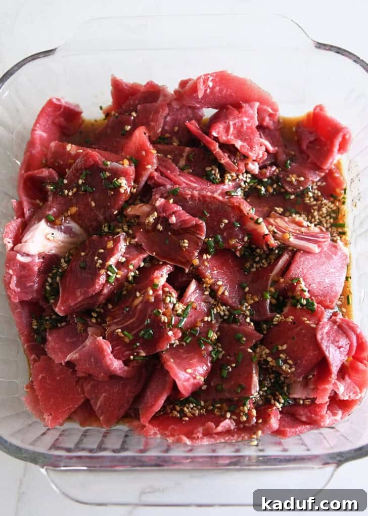 Simple Korean Beef Bulgogi 5 Top down view of square baking dish with thinly sliced beef and soy sauce, green onions and sesame seeds.