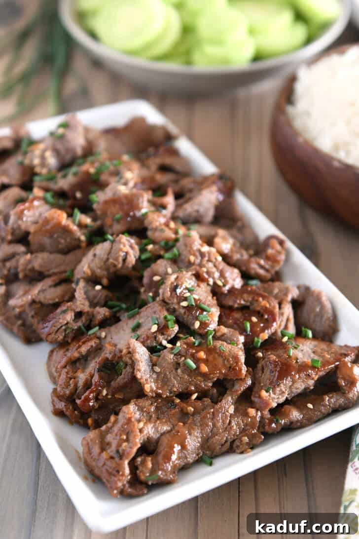 Simple Korean Beef Bulgogi 9 White tray with pieces of cooked beef, Korean sauce, green onions and sesame seeds.