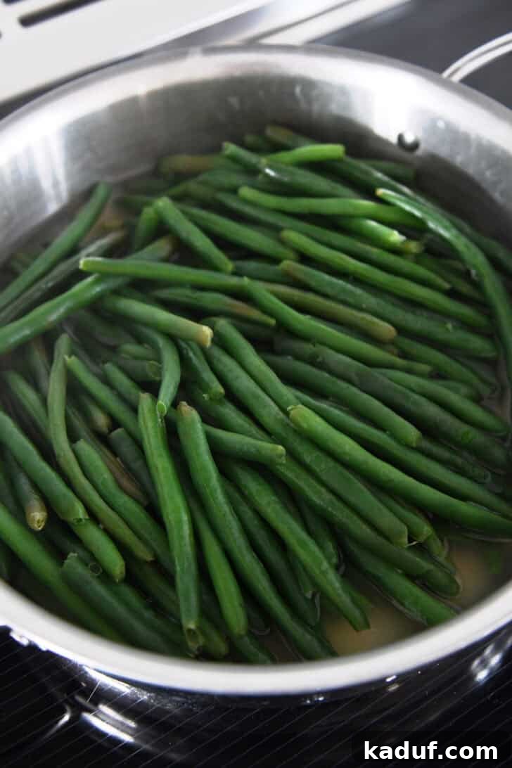 Simple Green Beans Almondine 3 Cooked green beans in chicken broth in skillet, showing the steaming process.