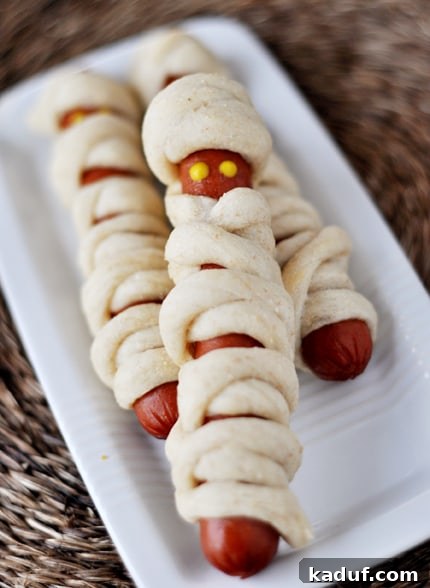 Monster Munchies Wrapped and Crawling 2 Hot dogs wrapped in breadstick dough to look like mummies on a white platter, ready for dipping.