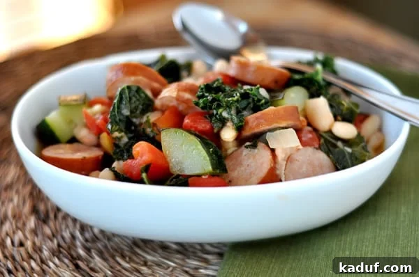 White oval bowl with savory white bean and sausage ragout, featuring kale, tomatoes, and zucchini.
