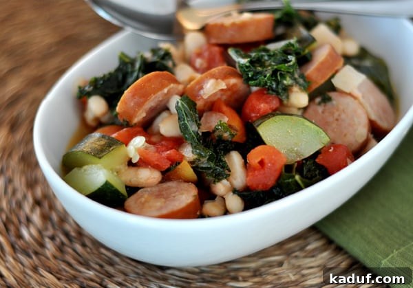 Top-down view of a white oval bowl generously filled with White Bean and Sausage Ragout, highlighting its vibrant colors and rich texture.