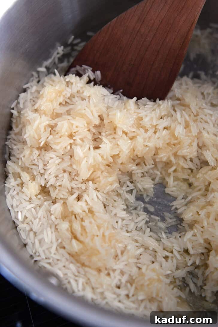 Fragrant Garlic Butter Rice 4 Uncooked rice cooking gently in melted butter within a stainless steel pot.