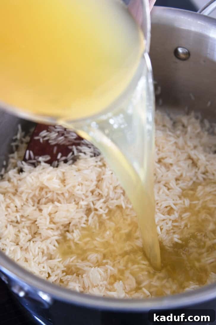 Fragrant Garlic Butter Rice 5 Pouring chicken broth into a pan containing butter-coated rice.