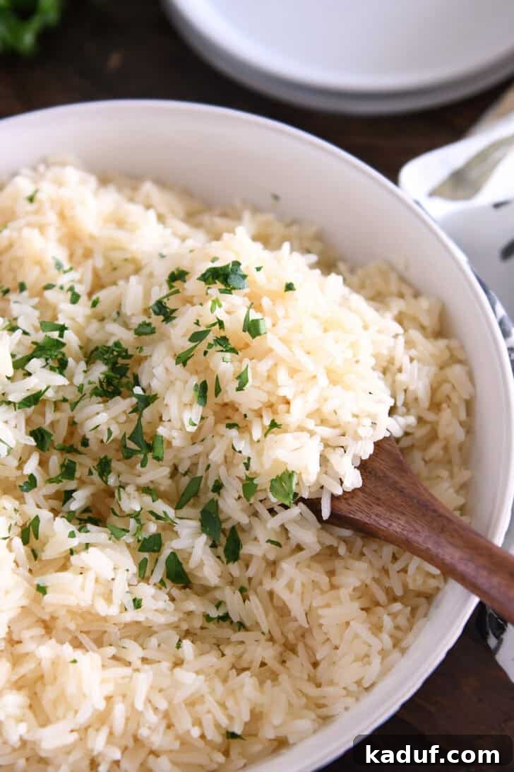 Fragrant Garlic Butter Rice 8 Wooden spoon scooping white rice with fresh parsley garnish from a white bowl.