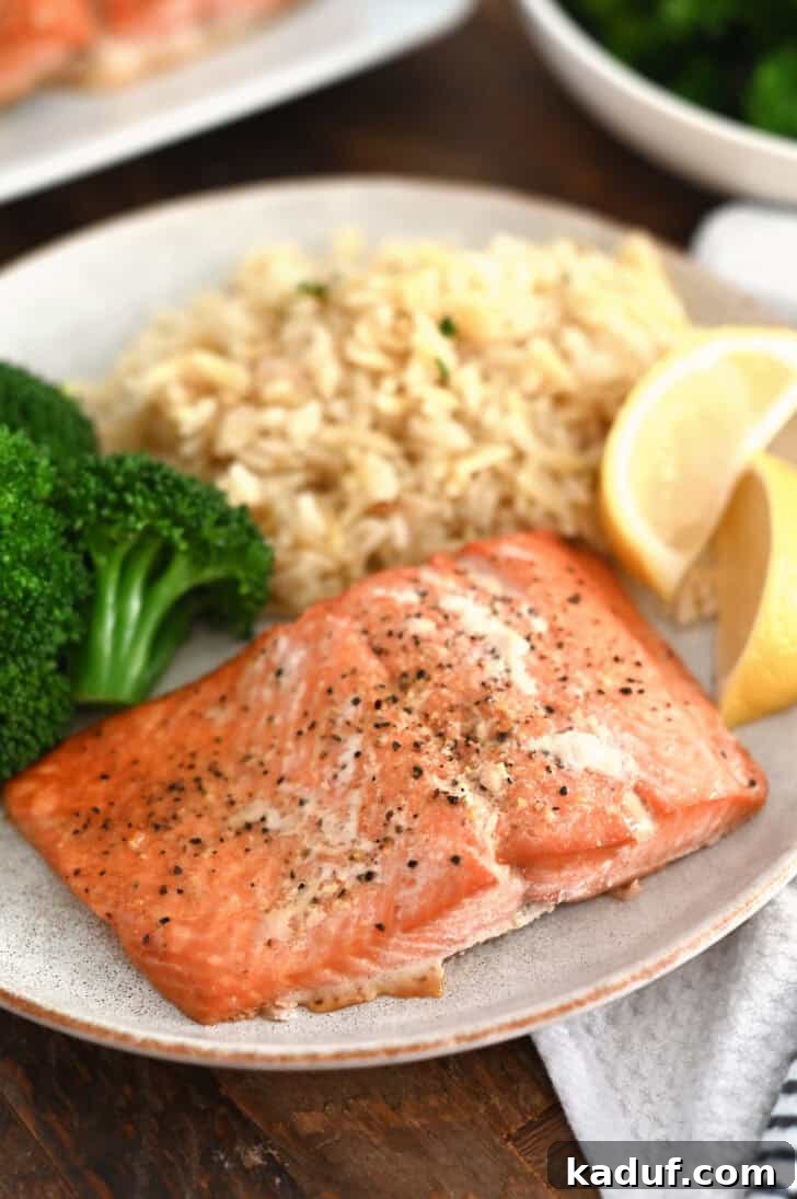 Ultimate Baked Salmon 2 Salmon filet on gray plate with lemon slices, cooked broccoli and rice pilaf.