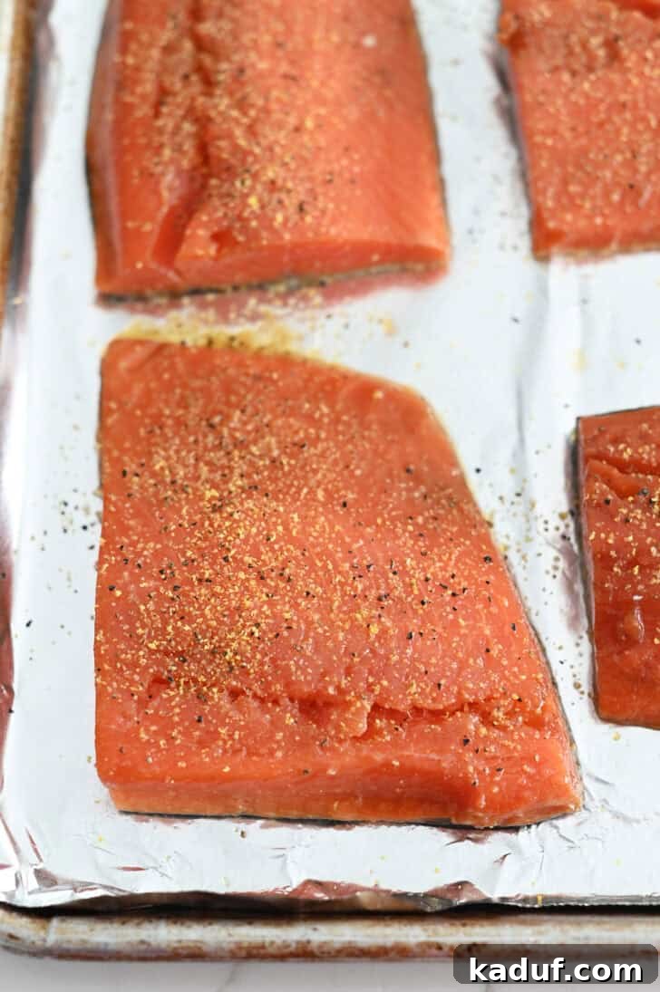 Ultimate Baked Salmon 5 Salmon filets sprinkled with lemon pepper seasoning on foil-lined baking sheet.