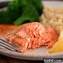 Salmon on gray plate with fork, lemon wedges, cooked broccoli and rice pilaf.