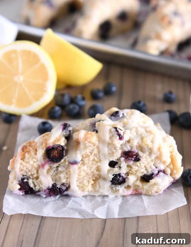 Irresistible Lemon Blueberry Scones 11 A single triangle-shaped lemon blueberry scone on crumpled white parchment paper, highlighting its texture.