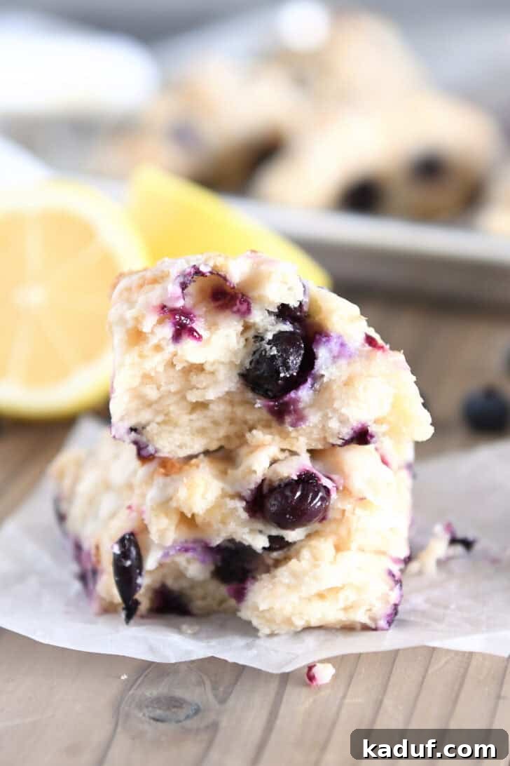 Irresistible Lemon Blueberry Scones 12 Two lemon blueberry scone halves stacked on white parchment paper, revealing the tender, flaky interior with blueberries.