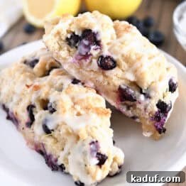 Irresistible Lemon Blueberry Scones 13 Two baked and glazed lemon blueberry scones on white plate, ready to be enjoyed.