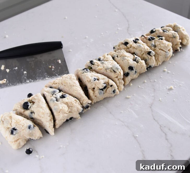 Irresistible Lemon Blueberry Scones 7 Scone dough expertly cut into triangle pieces on a floured surface with a bench scraper.