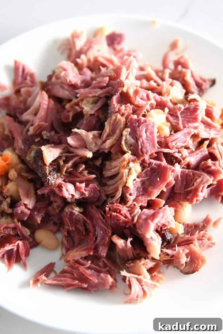 Hearty Slow Cooked Ham and Bean Soup 6 A pile of perfectly shredded ham pieces resting on a pristine white plate, ready to be added back to the soup.