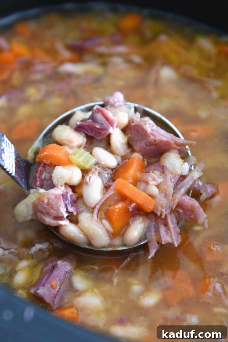 Hearty Slow Cooked Ham and Bean Soup 7 A ladle holding a spoonful of rich ham and bean soup, showcasing tender white beans, carrots, celery, and savory ham pieces in a flavorful broth.