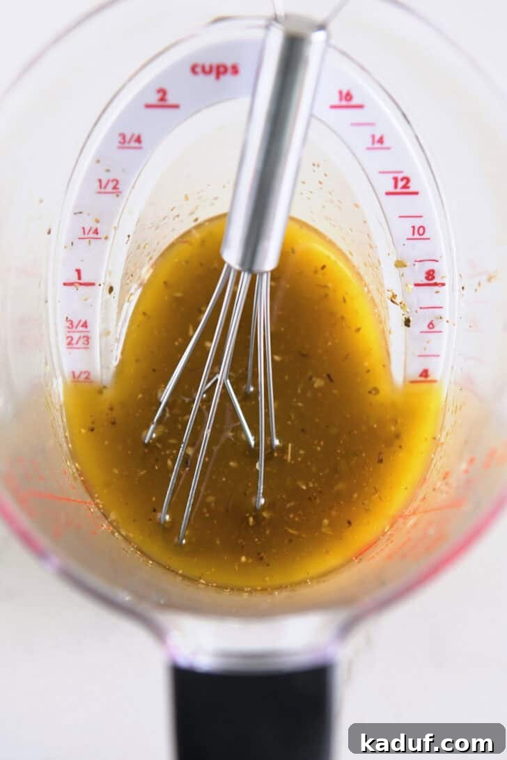 Liquid measuring cup with a rich blend of olive oil, fresh lemon juice, aromatic oregano, and finely minced garlic, prepared for the chicken souvlaki marinade.