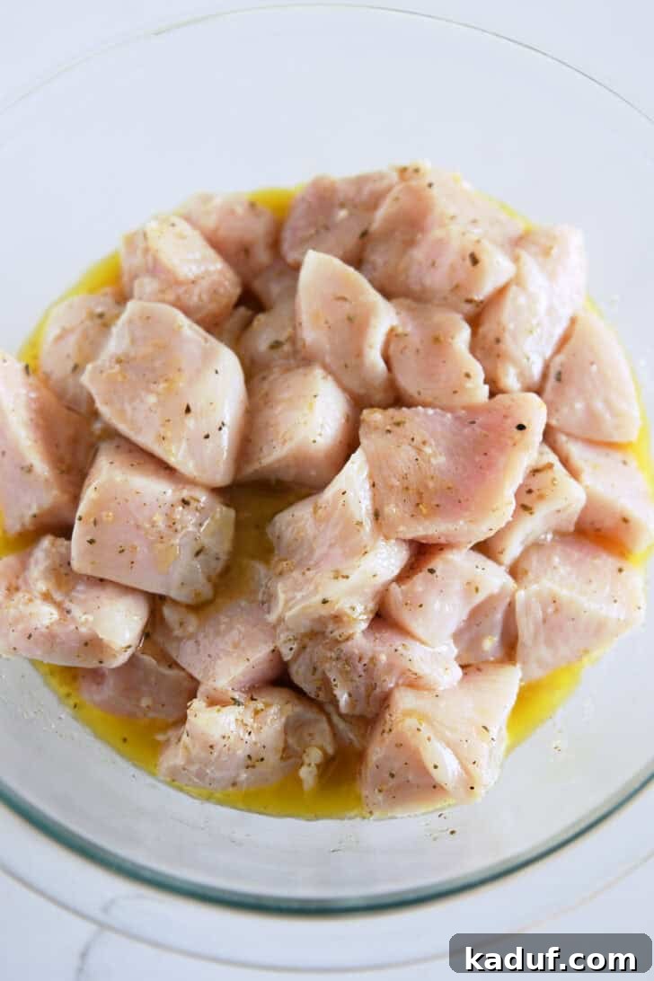 Glass bowl containing bite-sized chicken pieces thoroughly coated and marinating in a vibrant mixture of lemon juice, olive oil, and oregano, infusing them with authentic Greek flavors.