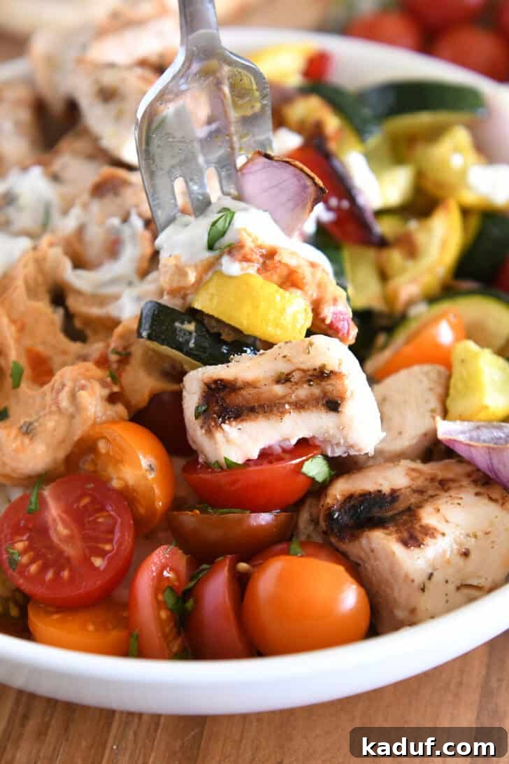 A close-up shot of a fork piercing a delectable bite, featuring tender chicken souvlaki, perfectly roasted vegetables, creamy hummus, and refreshing tzatziki sauce, highlighting the harmonious blend of flavors and textures in the bowl.