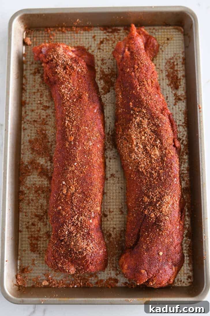 Quick and Tender Air Fryer Pork Tenderloin 4 Two perfectly spice-crusted pork tenderloins, ready for the air fryer, resting on a glistening gold baking sheet.