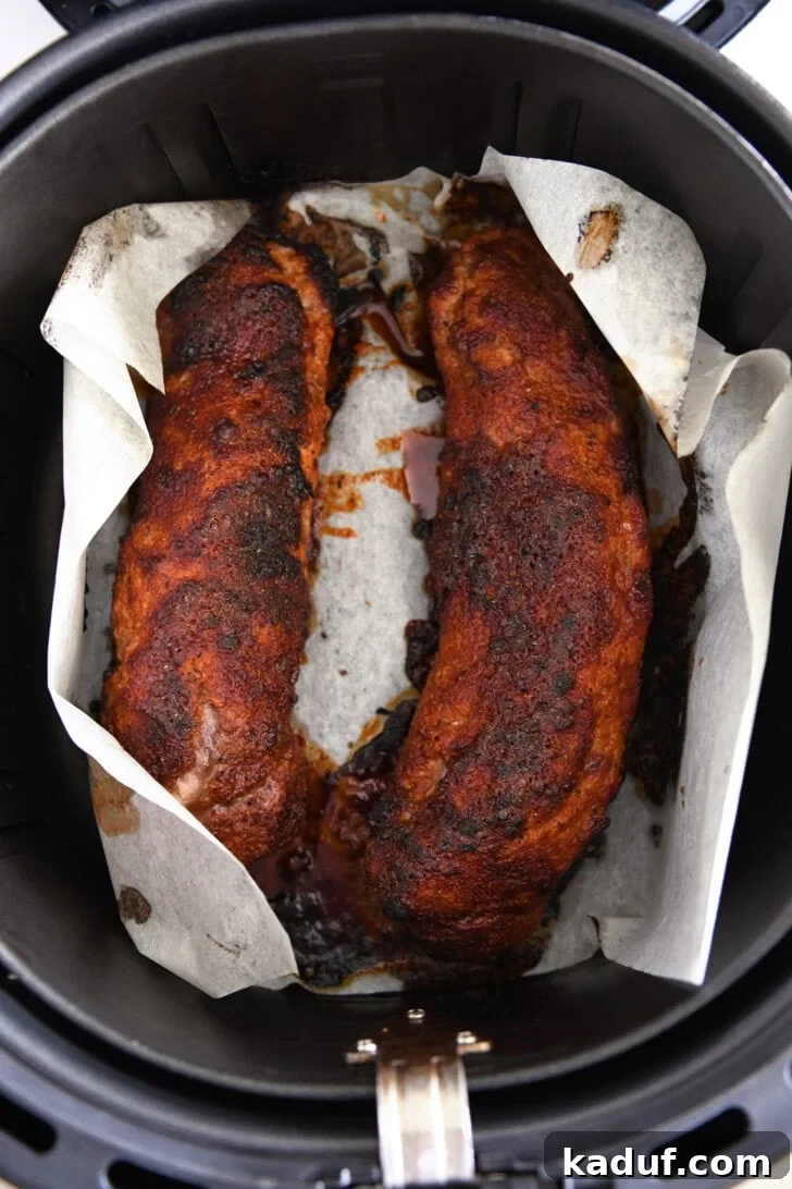 Quick and Tender Air Fryer Pork Tenderloin 6 The two pork tenderloins perfectly browning on parchment paper within the air fryer, midway through cooking.