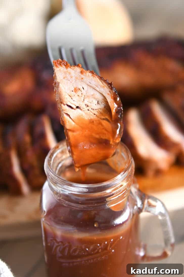 Quick and Tender Air Fryer Pork Tenderloin 8 A fork piercing a succulent piece of cooked pork tenderloin, glistening with BBQ sauce, ready to be enjoyed.