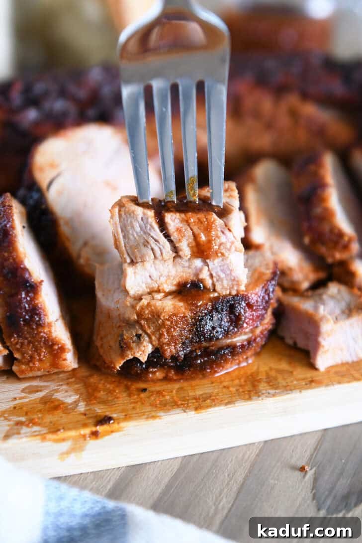 Quick and Tender Air Fryer Pork Tenderloin 9 A fork delicately piercing two stacked, perfectly cooked slices of pork tenderloin on a clean wood cutting board, highlighting its tenderness.